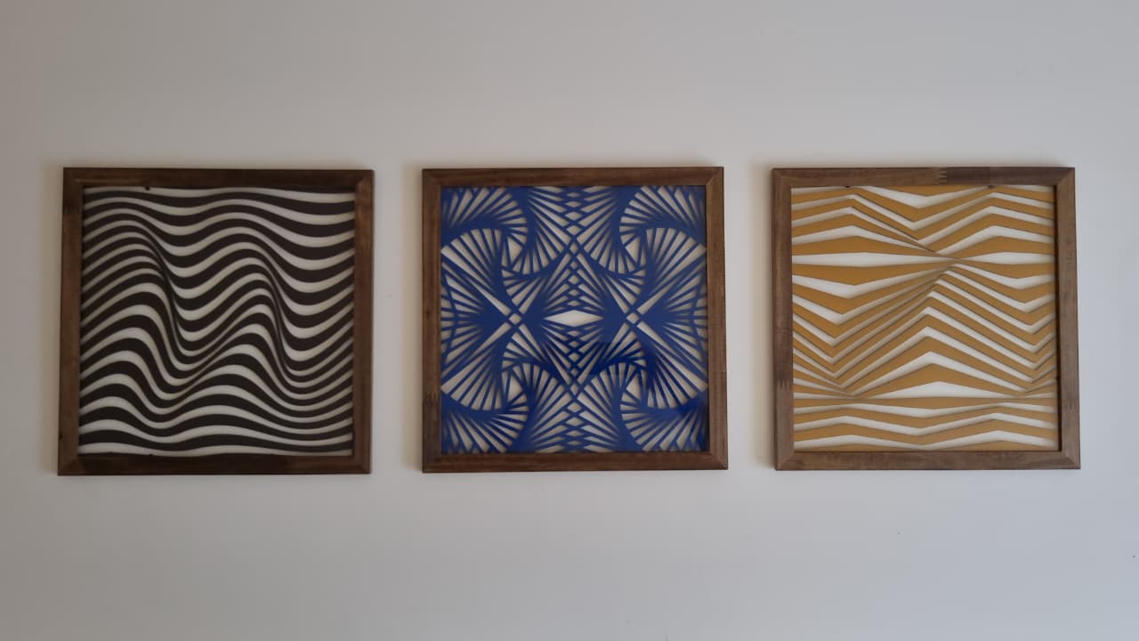 Três obras geométricas emolduradas, em preto e branco, azul e branco, e dourado e branco, feitas nas cores escolhidas pela cliente